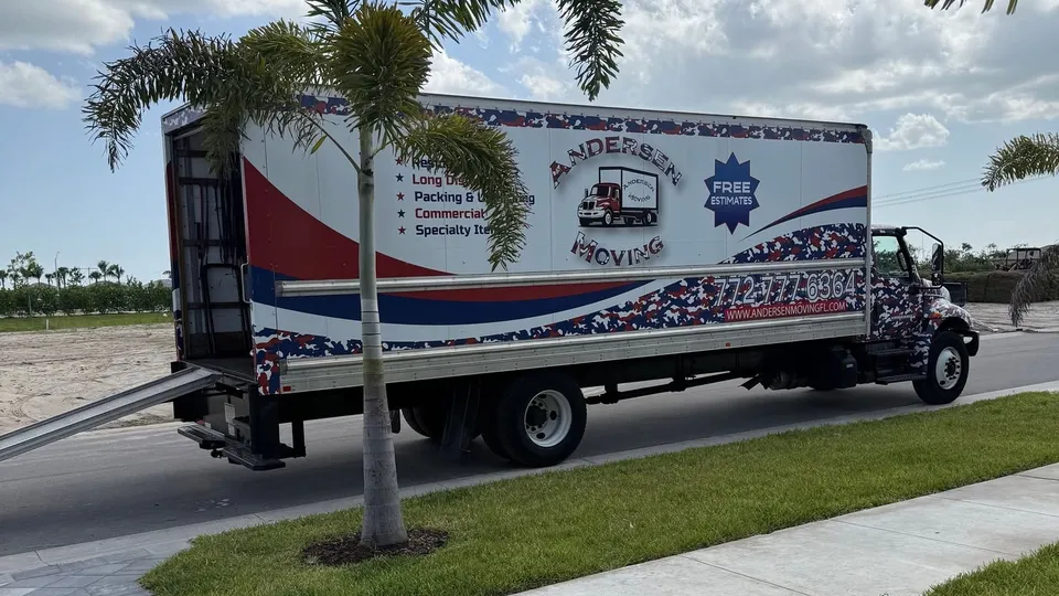 Andersen Moving box truck with its loading ramp down on a Treasure Coast street beside a young palm tree.